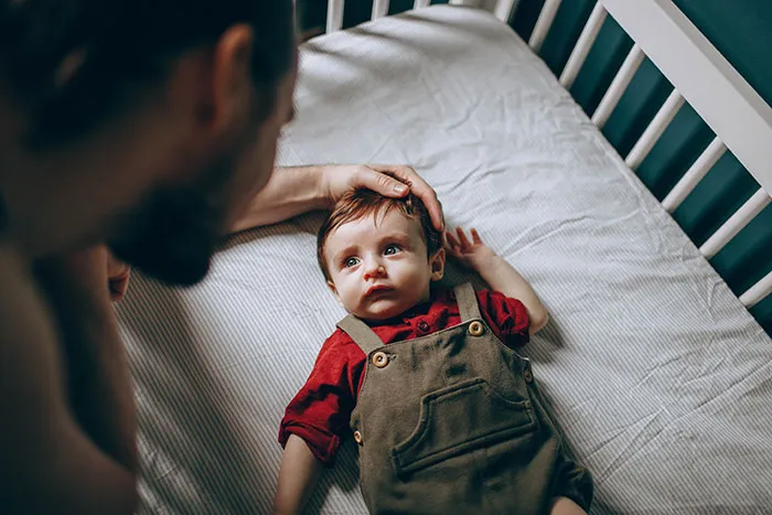 Man stroking baby in cot