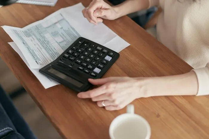 Woman using a vintage calculator, an old gadget that was a trendsetter of its time on a wooden table with documents nearby