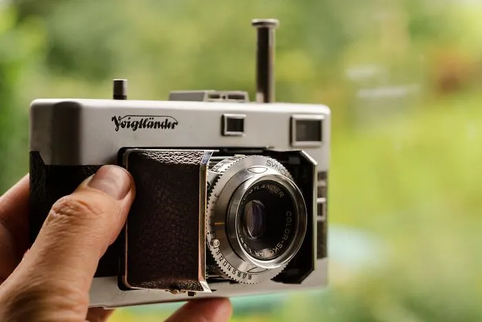Person holding an old film camera, showcasing vintage gadgets that were trendsetters of their time in technology history.