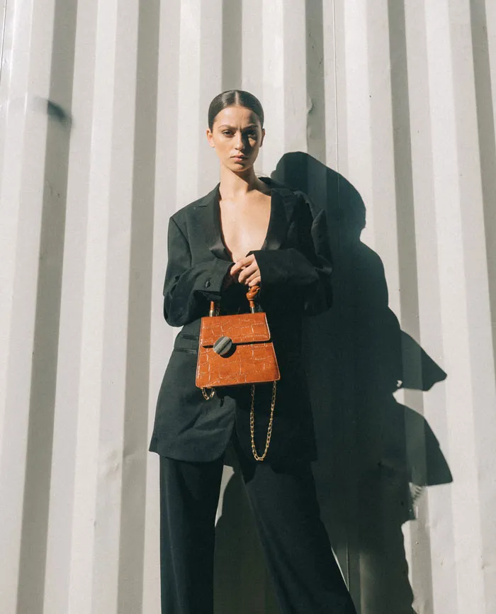 Woman standing wearing black outfit and holding brown bag
