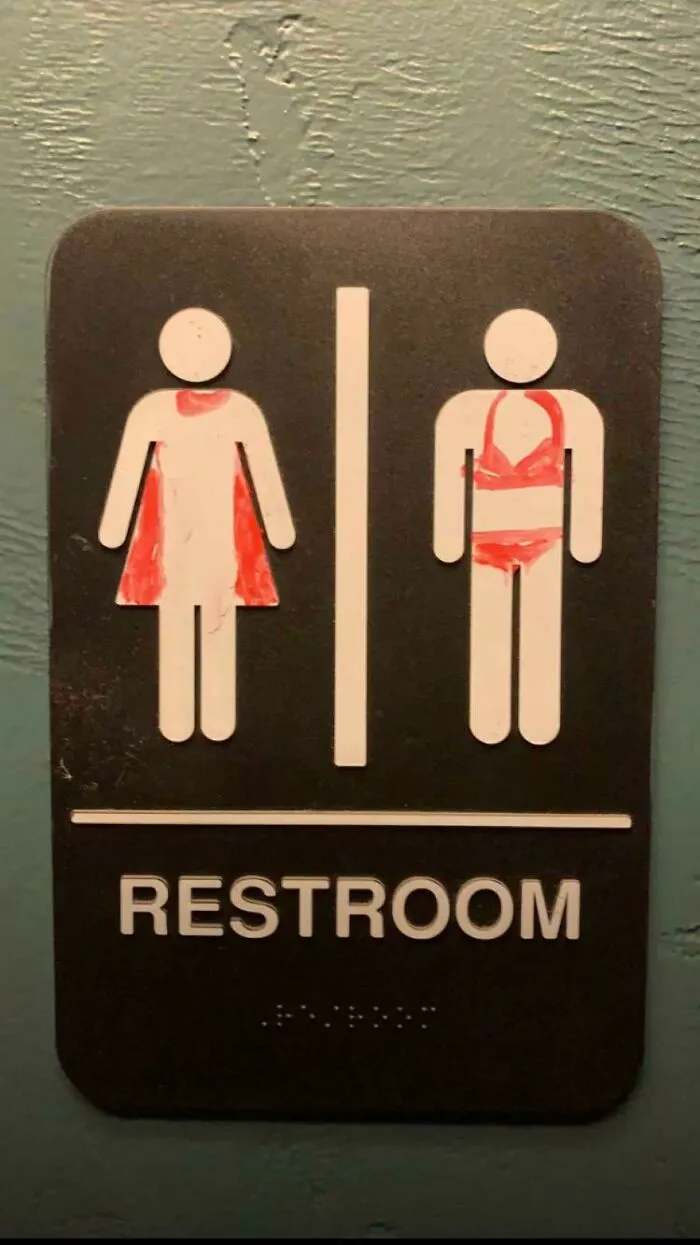 Un letrero de baño vandalizado de forma muy moderada, considerando que ha sido pintado con un marcador para pizarra 