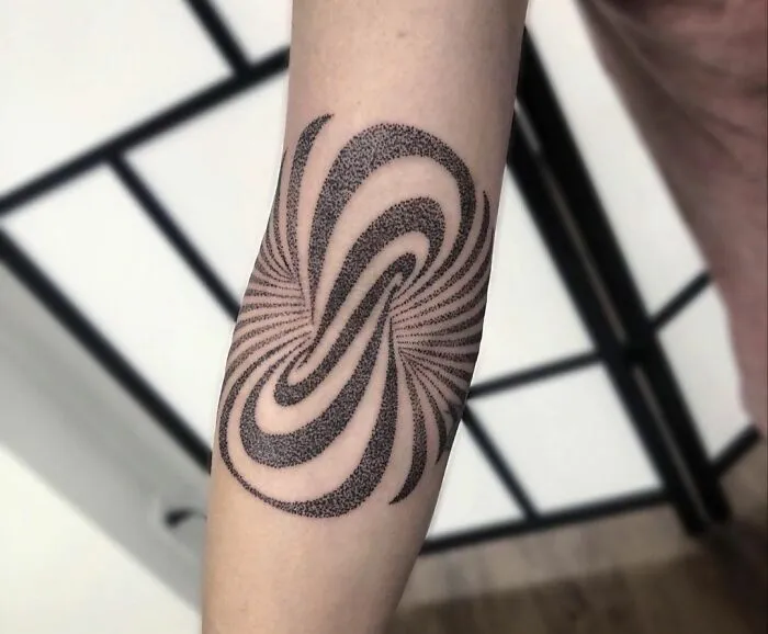Optical illusion tattoo design on forearm creating a swirling effect with intricate dot patterns.