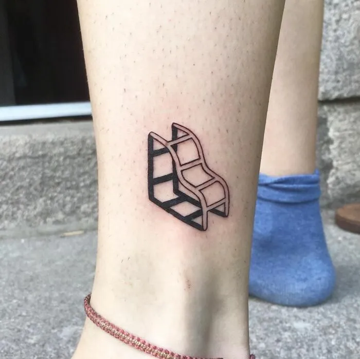 Optical illusion tattoo design on leg, featuring an impossible stair motif in black ink.