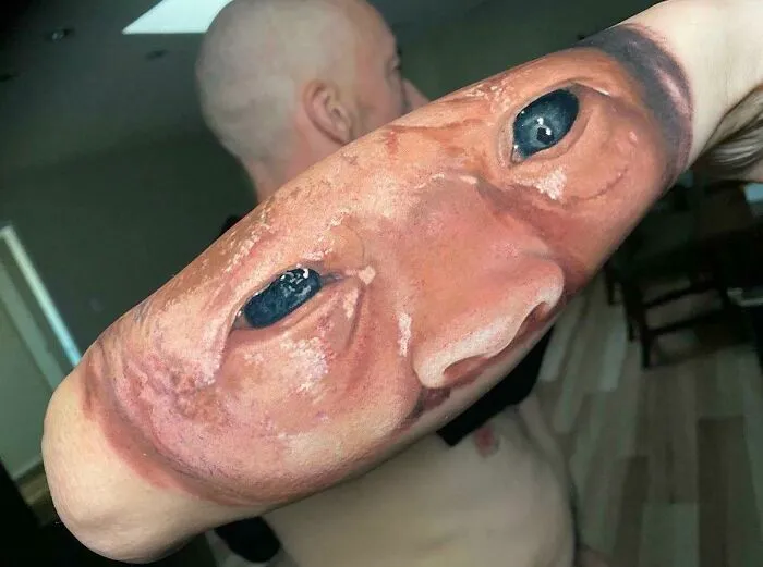 Forearm tattoo depicting a realistic human face, showcasing a unique and permanent inked mistake.
