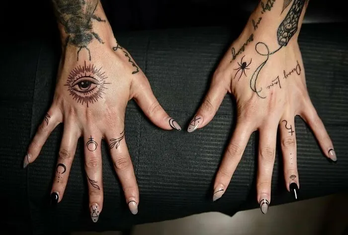 Small hand tattoos with intricate designs on both hands, featuring symbols and an eye motif.