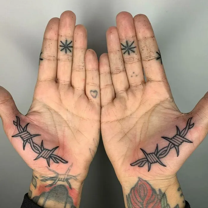 Small hand tattoos featuring barbed wire designs and minimalist symbols on both palms.
