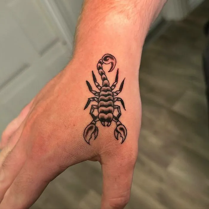 Small hand tattoo of a scorpion on the back of a person's hand.