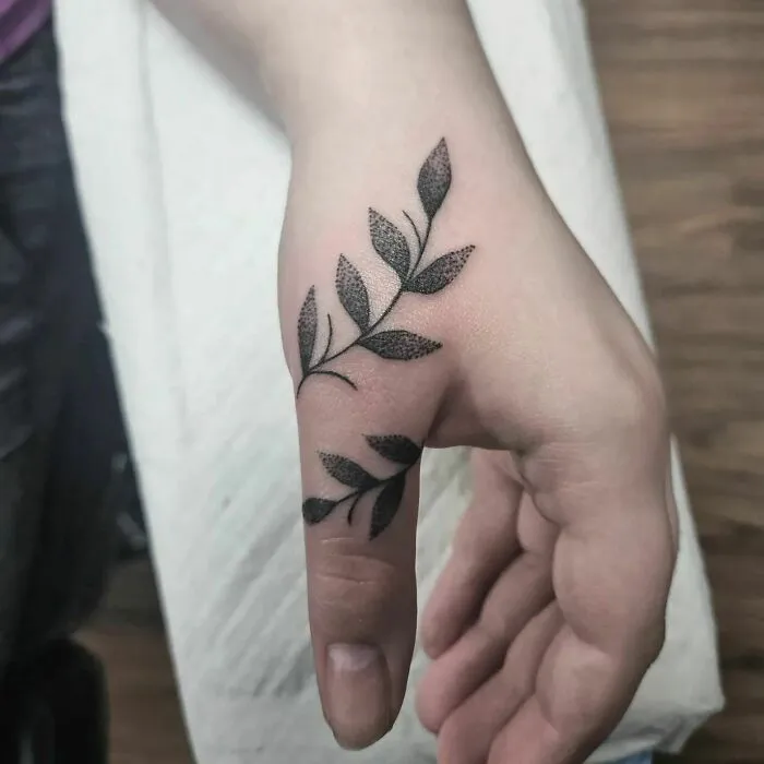 Leaf design small hand tattoo on a person's thumb and wrist.