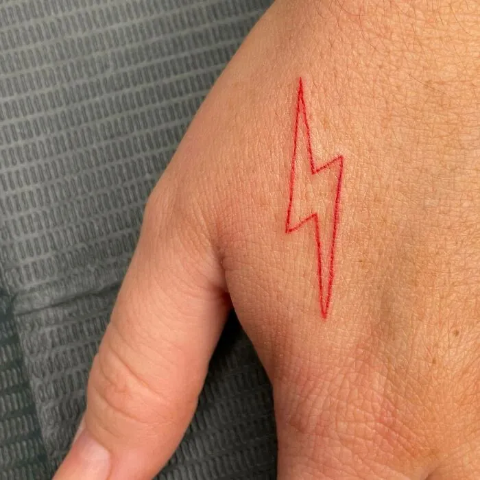 Small hand tattoo featuring a red lightning bolt design on the back of a hand.