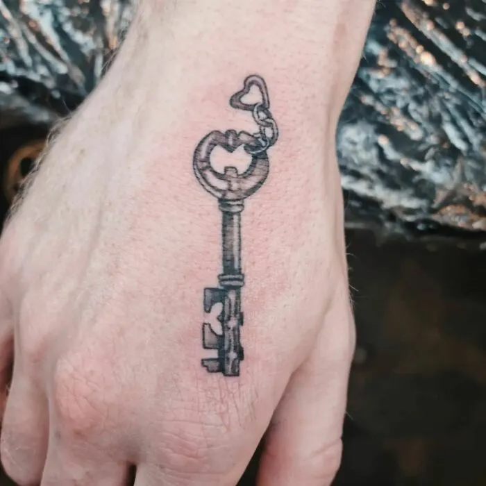 Small hand tattoo featuring a detailed skeleton key design.