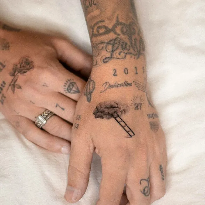 Close-up of small hand tattoos featuring various designs, including a rose, ladder, and numbers.