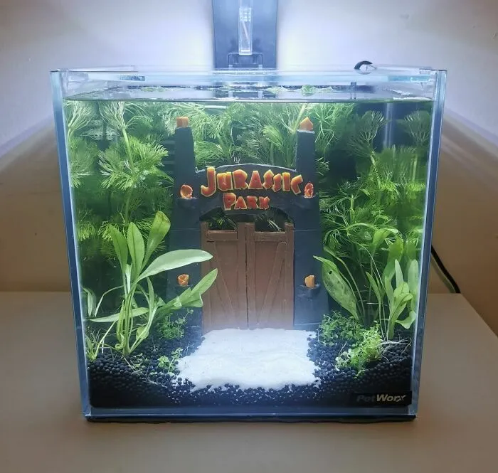 Creative aquarium design with a "Jurassic Park" theme, featuring lush green plants and a miniature entrance gate.