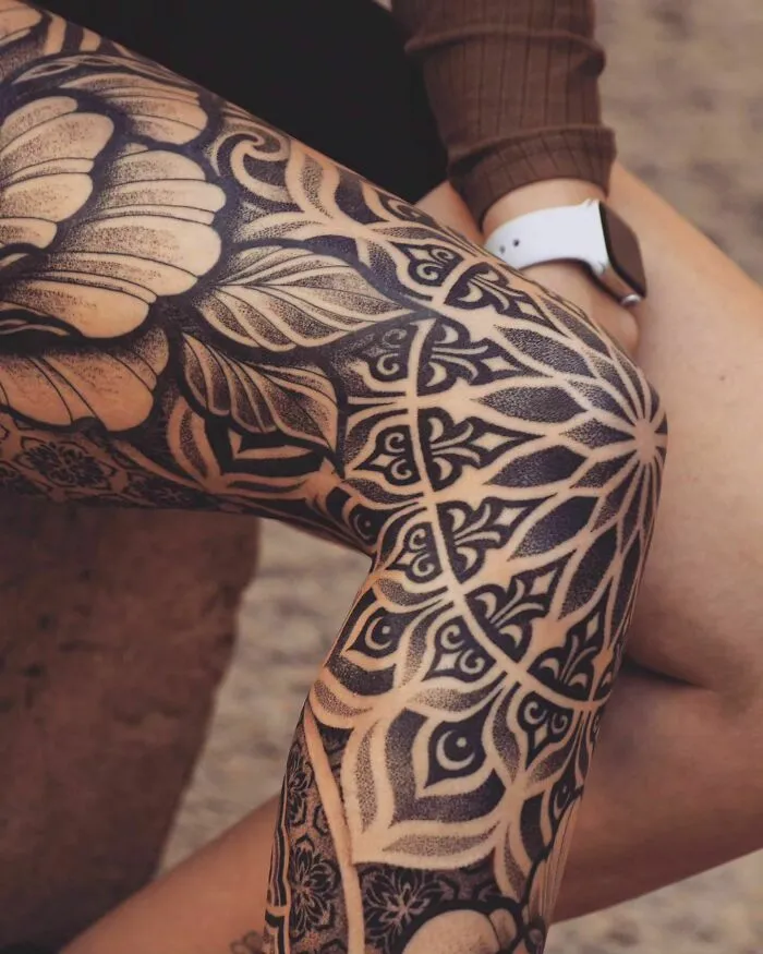 Intricate geometric knee tattoos with bold black ink and floral patterns on legs.