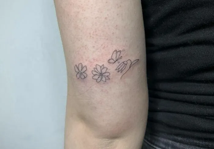 Minimalist flower tattoo on arm with butterfly, showcasing elegance and beauty.