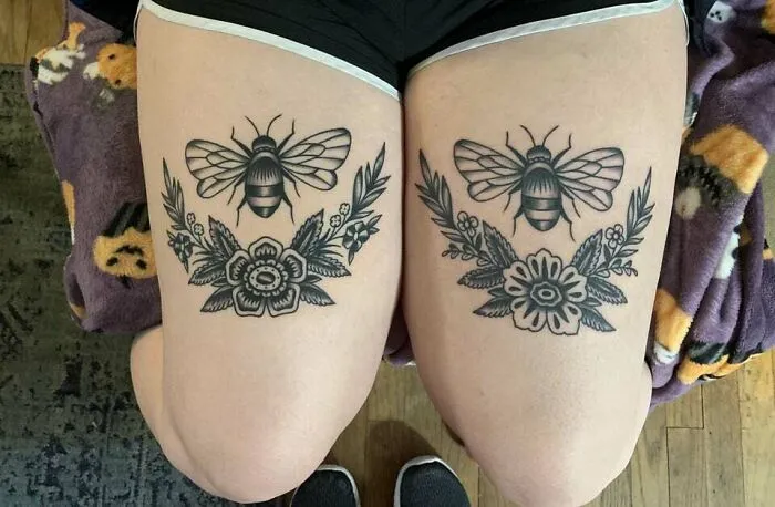 Bee and floral knee tattoos on person's legs, featuring detailed black ink designs.