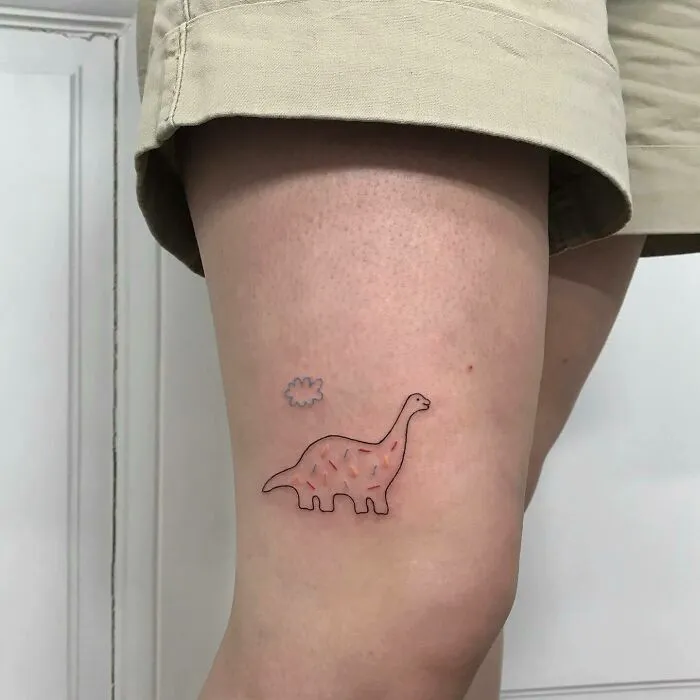 Knee tattoo featuring a cute dinosaur and cloud design, showcasing unique ink art on a person's leg.