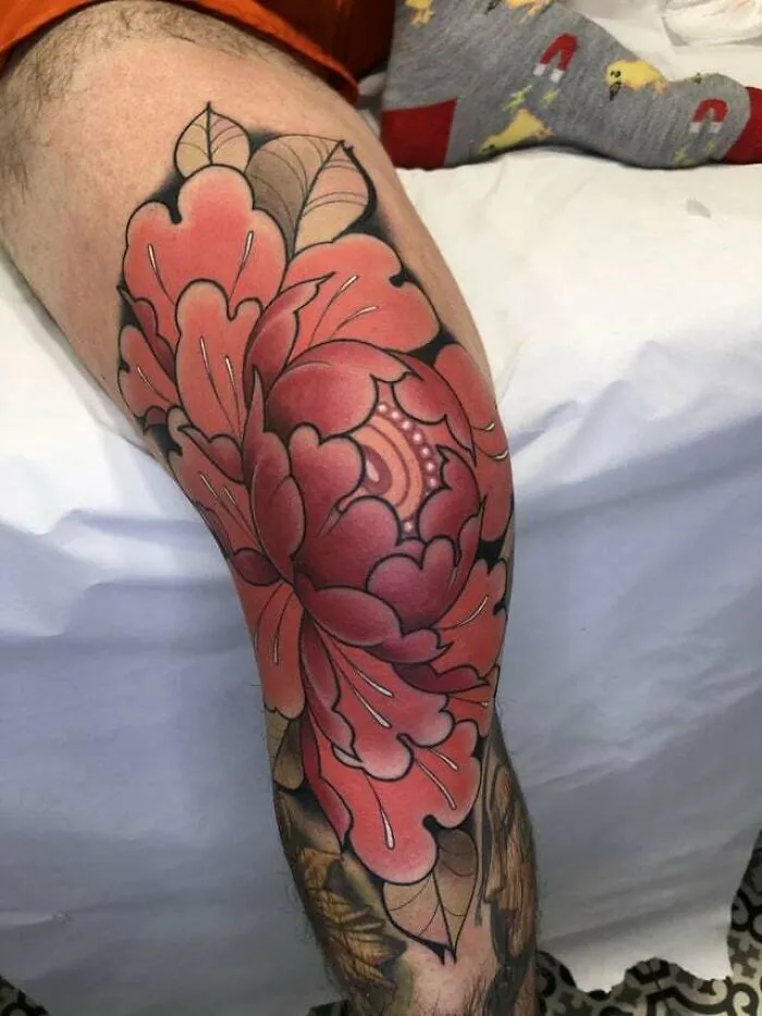 Colorful knee tattoo featuring a large floral design with bold outlines and intricate details.