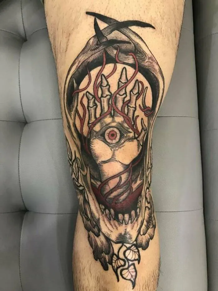Intricate knee tattoo design featuring an eye, flames, and skeletal fingers.