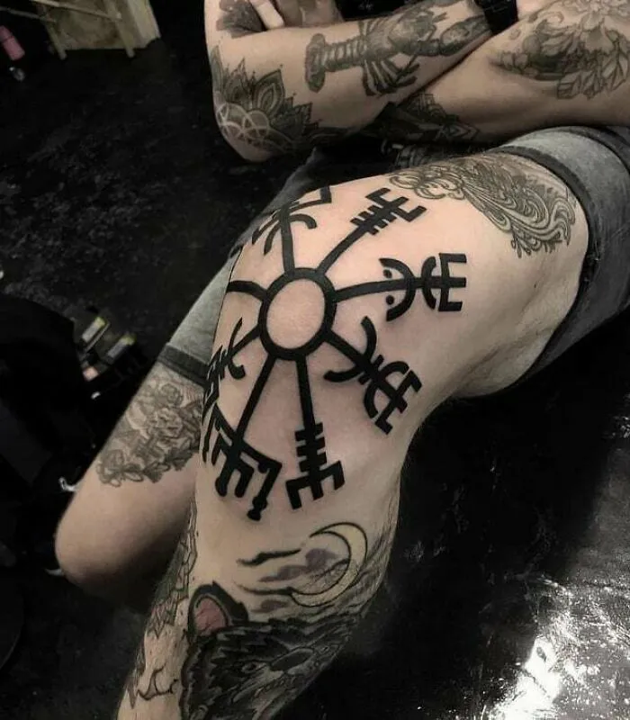 Intricate knee tattoo with bold, geometric design, surrounded by other tattoos on the leg.