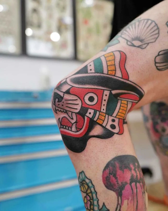 Colorful Aztec-inspired knee tattoo design showcasing bold, geometric patterns with animal motifs.