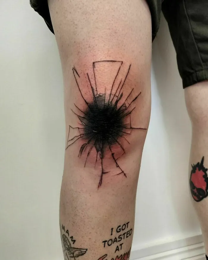 Knee tattoos with a cracked glass design in black, surrounded by other smaller leg tattoos.