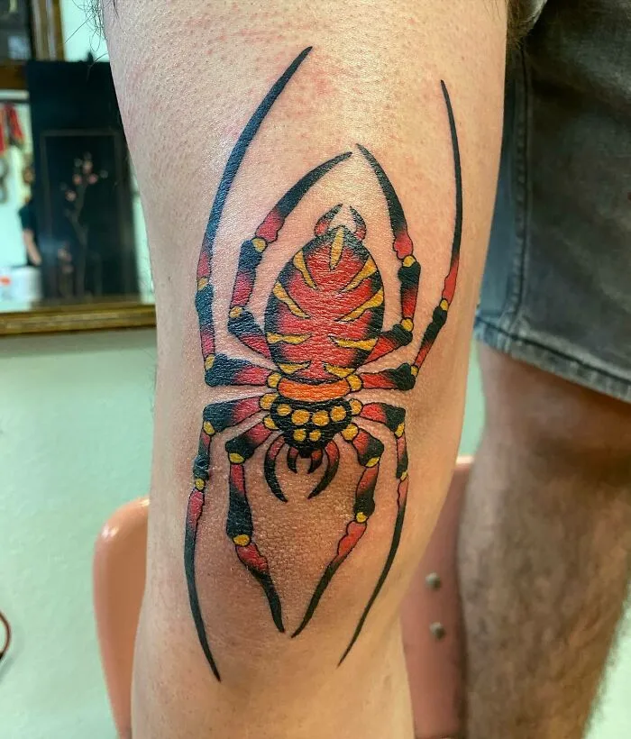 Colorful spider knee tattoo design on leg, showcasing bold artwork in a tattoo studio.