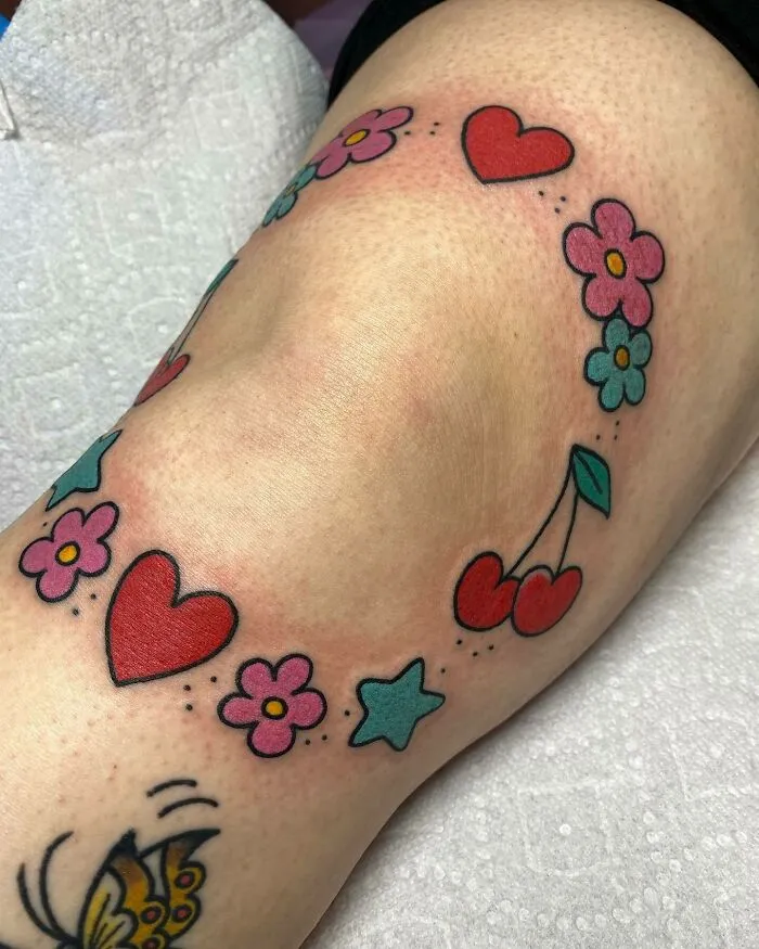 Colorful knee tattoo with hearts, flowers, stars, and cherries design.