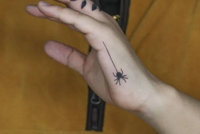 Small hand tattoo of a black spider on the palm, with minimalist design and detail.