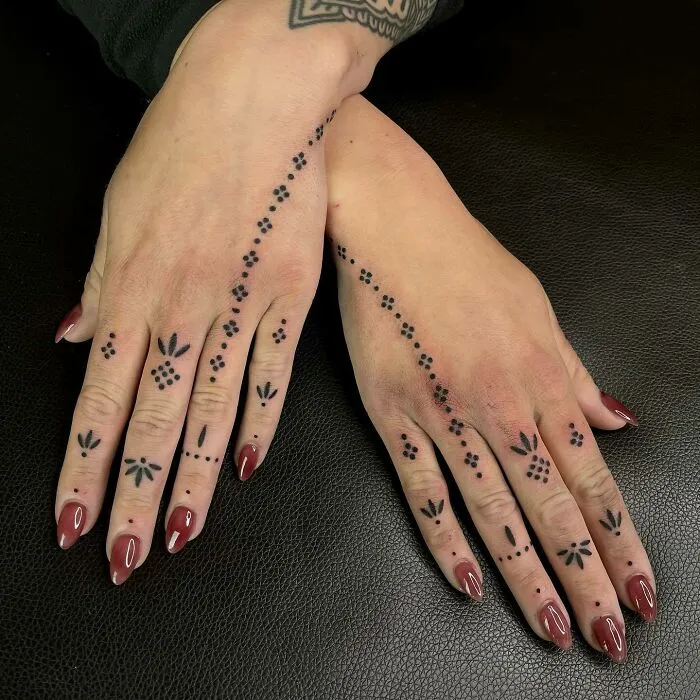 Small hand tattoos with geometric and floral designs on both hands.