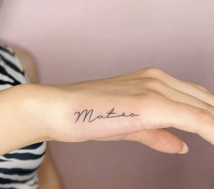 Small hand tattoo with the name "Mateo" in elegant script.