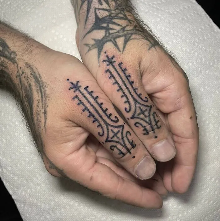 Intricate small hand tattoos with geometric and star designs on the fingers.