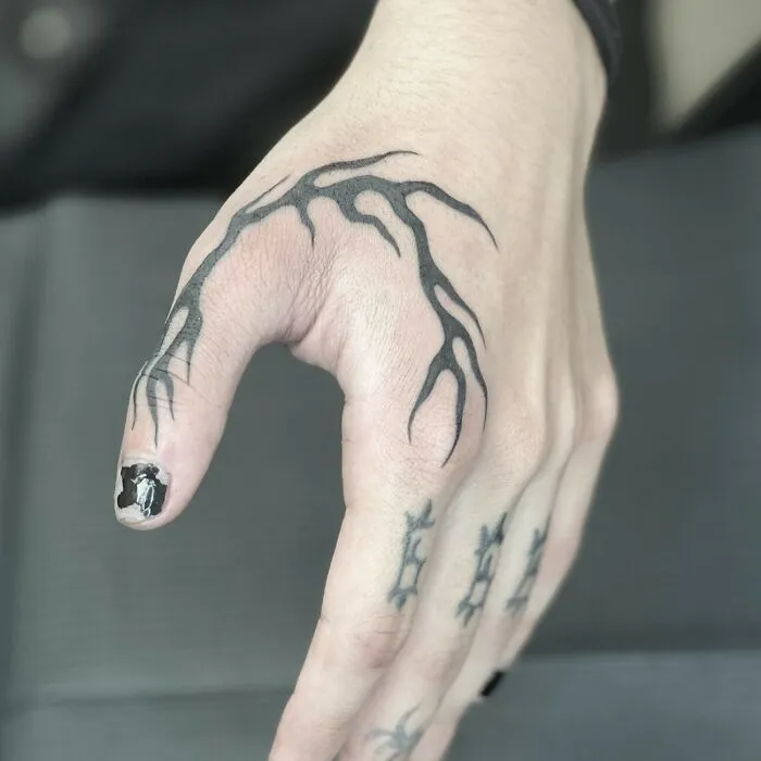 Unique small hand tattoos featuring intricate black vine designs on the fingers and thumb.
