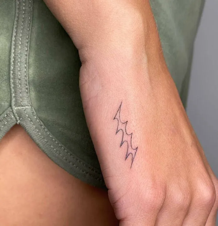 Minimalist small hand tattoo of abstract wavy lines on a person's hand, in close-up view.
