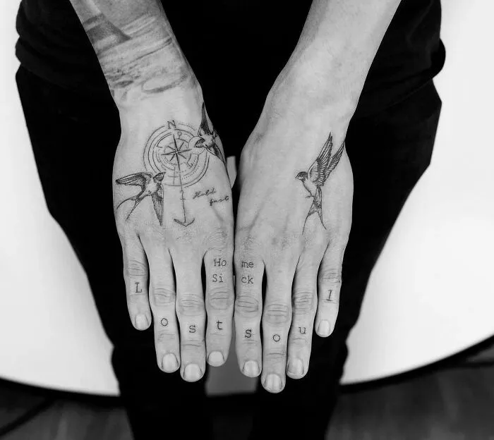 Small hand tattoos featuring birds and compass with the words "Lost Soul" and "Home Sick" on fingers.