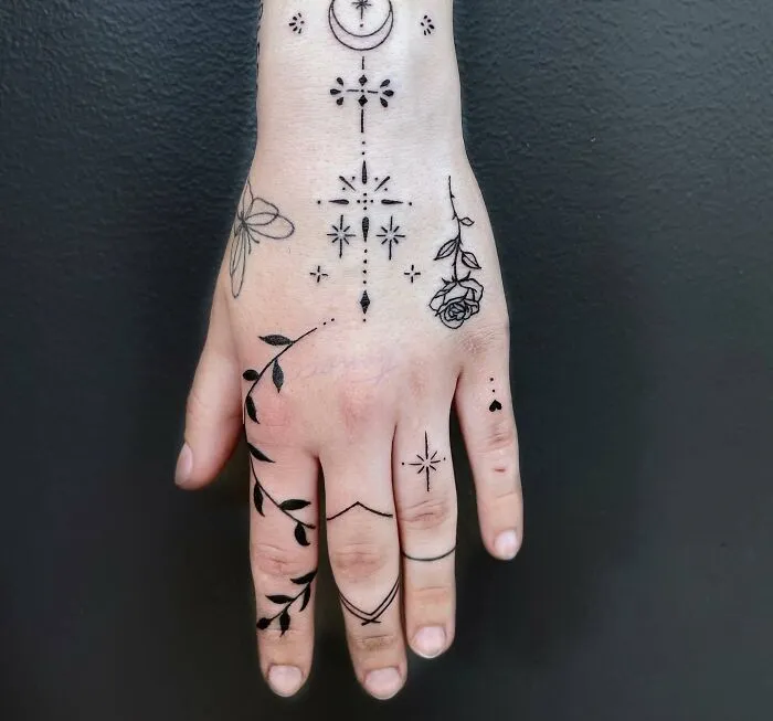 Small hand tattoos featuring a mix of floral and geometric designs on a hand against a black background.