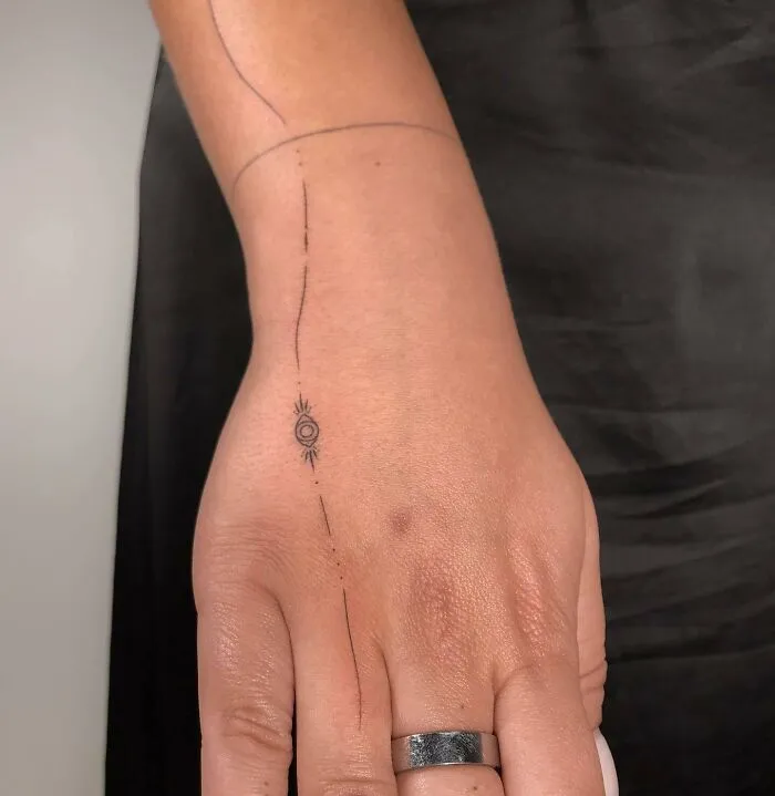 Minimalist small hand tattoo with an eye design on the wrist.