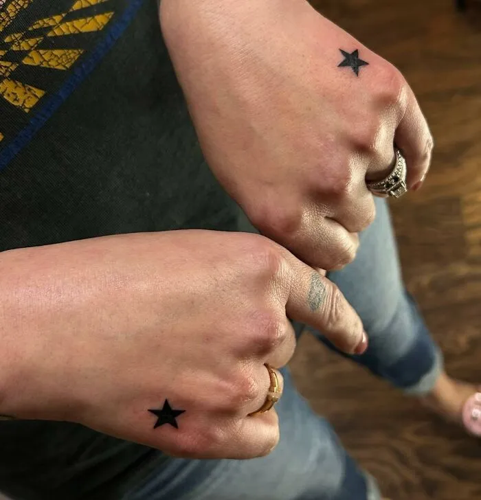 Two small hand tattoos featuring black stars on the back of each hand.