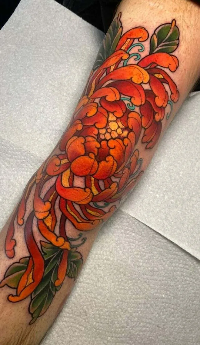 Vibrant chrysanthemum tattoo design on a leg, showcasing bold colors and intricate details.