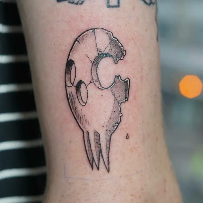 Unique anime tattoo design featuring a cracked mask on forearm.