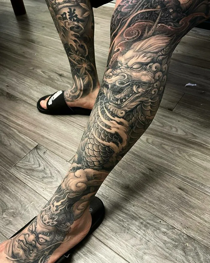 Detailed black and gray dragon tattoo covering a leg, featuring scales and fierce eyes.