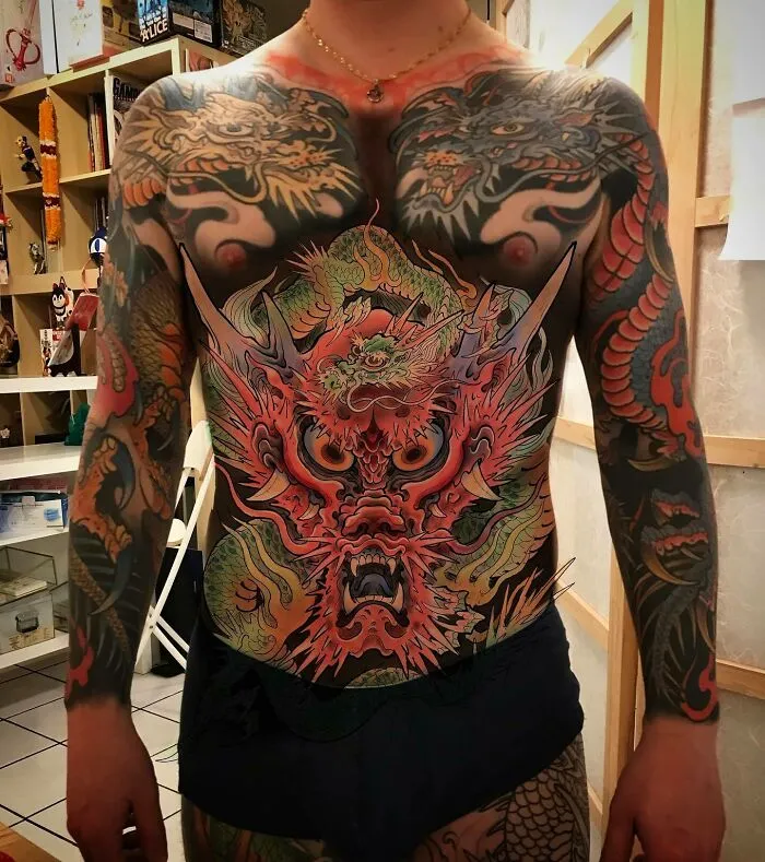 Colorful dragon tattoo covering a person's chest and arms, showcasing intricate designs and vibrant hues.