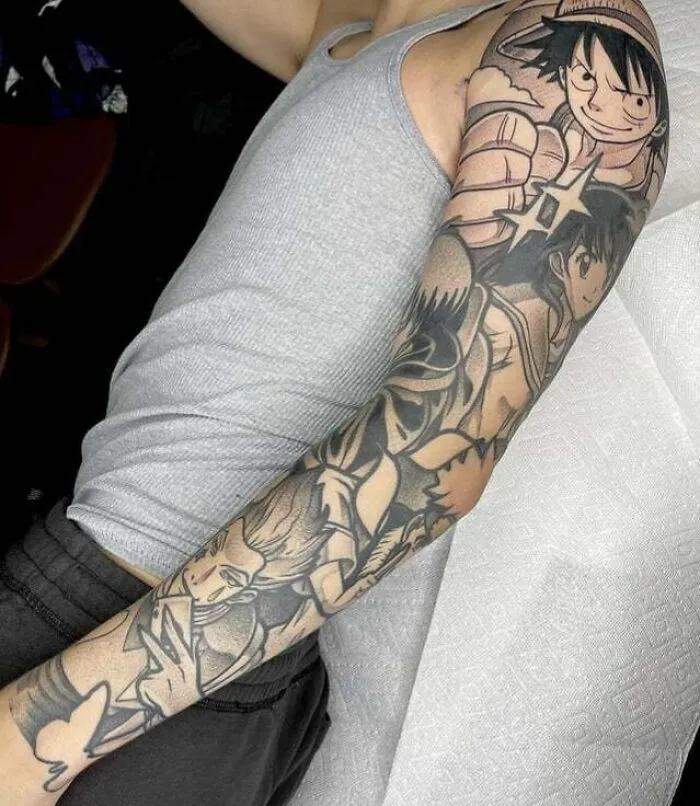 Arm with intricate anime tattoo sleeves featuring popular characters, showcasing detailed and cool designs in black ink.