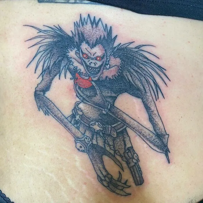 Anime tattoo featuring a detailed character with red eyes and distinct features, showcasing intricate ink artistry.