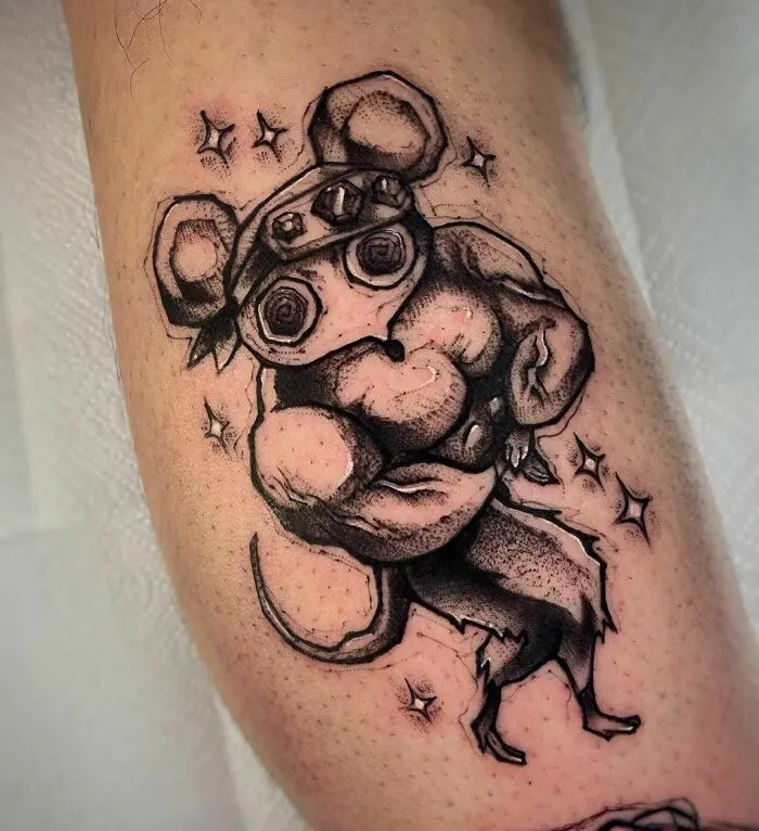 Muscular anime character tattoo with goggles and mouse ears on arm.