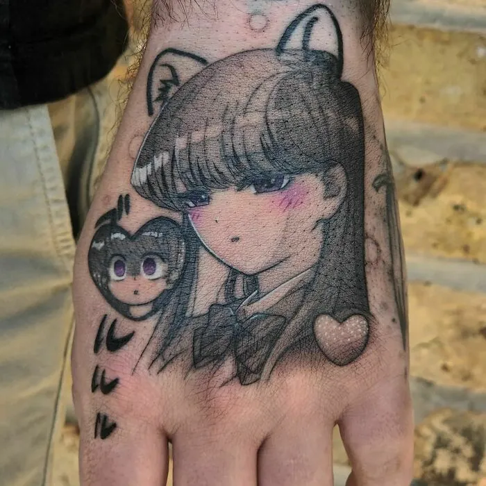 Anime tattoo of a character with long hair and cat ears, inked on a hand, featuring a heart and smaller portrait.