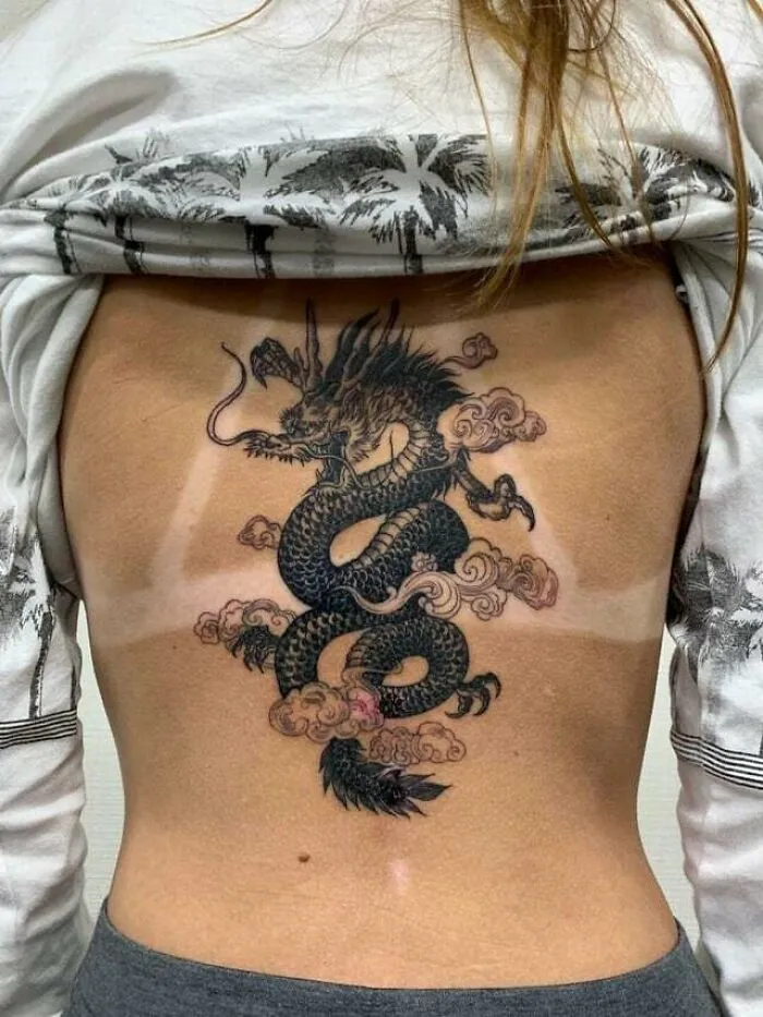Intricate dragon tattoo on a person's back, featuring detailed scales and clouds, embodying fiery artistic expression.