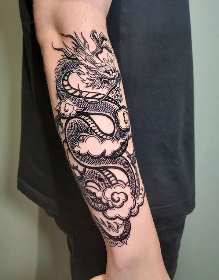 Dragon tattoo on forearm, with intricate black ink design featuring clouds and scales.