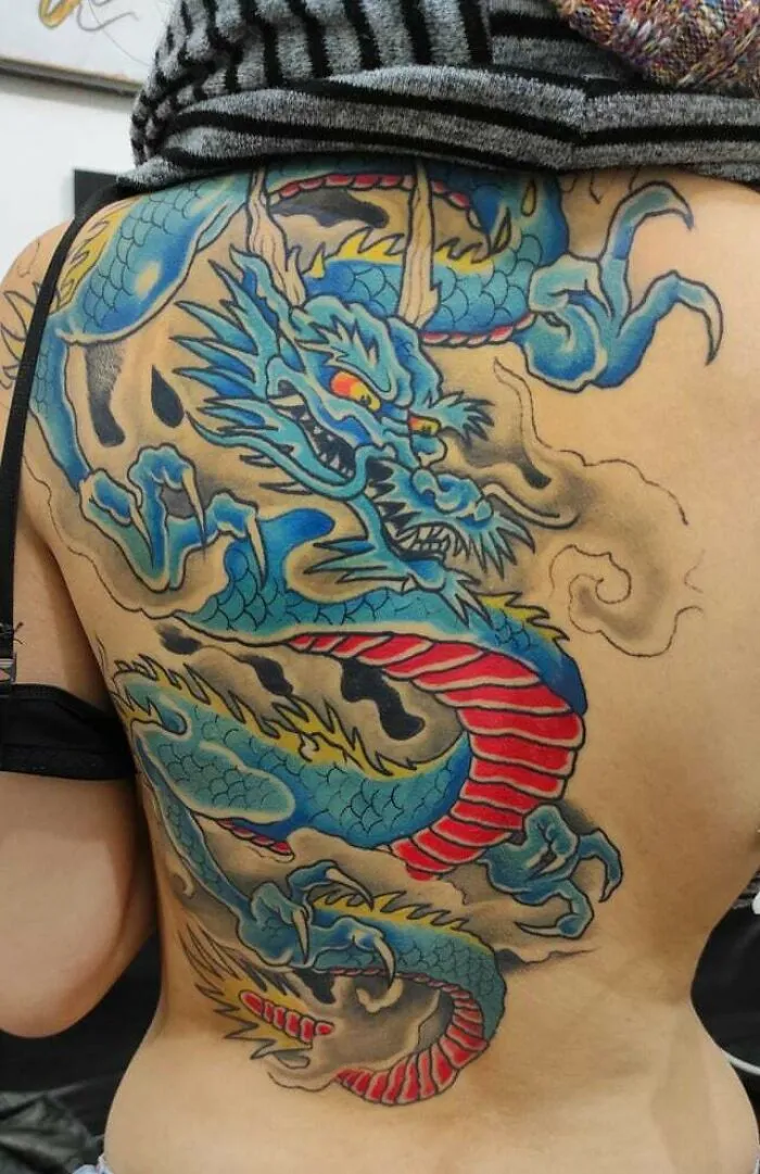 Vibrant dragon tattoo design with blue and red tones on a person's back.