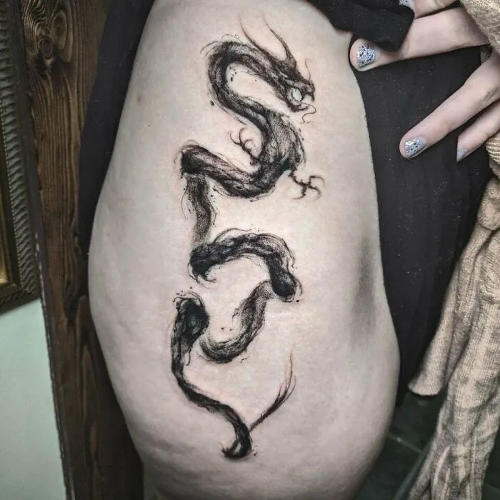 Ink brush style dragon tattoo on thigh, showcasing unique design elements.