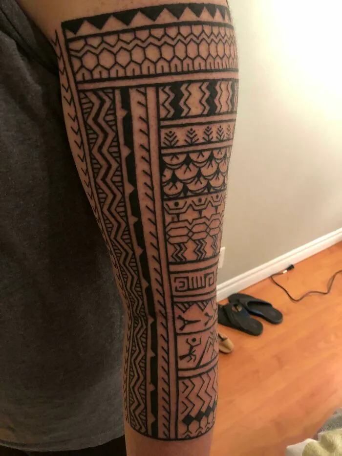 Arm with a detailed tribal tattoo design featuring intricate geometric patterns and symbols.